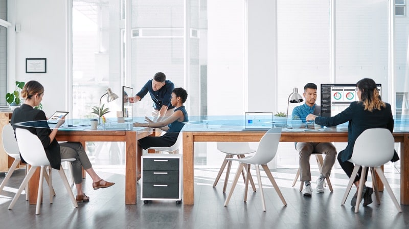 A modern office with five people looking at the devices. ASUS business software is shown on the screen.