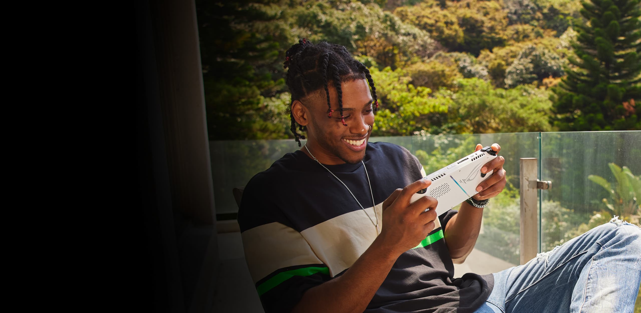 Person sitting on a chair outside and smiling while playing with the ROG Ally.